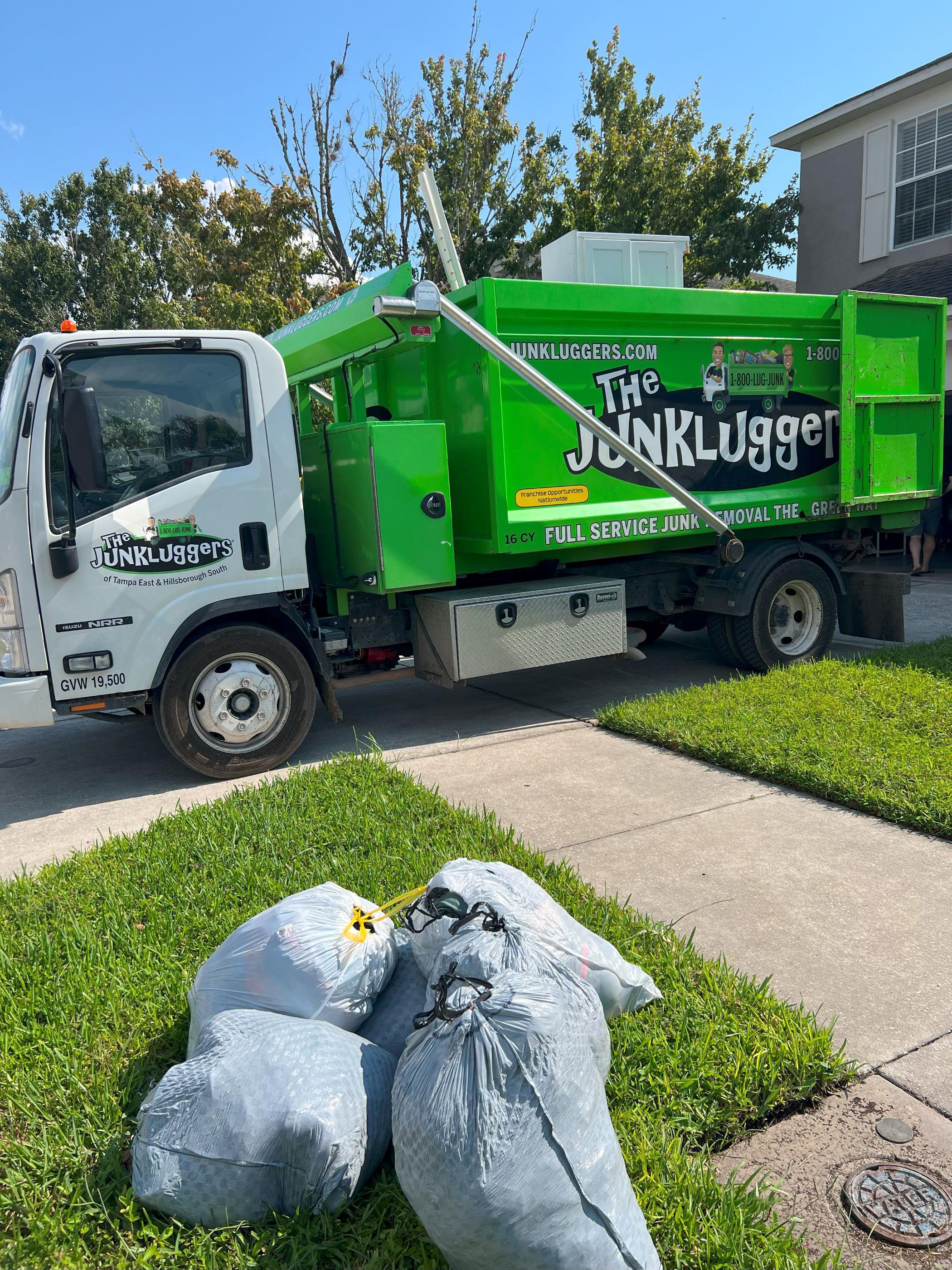 Junkluggers truck parked by curb with bags of junk ready for pickup
