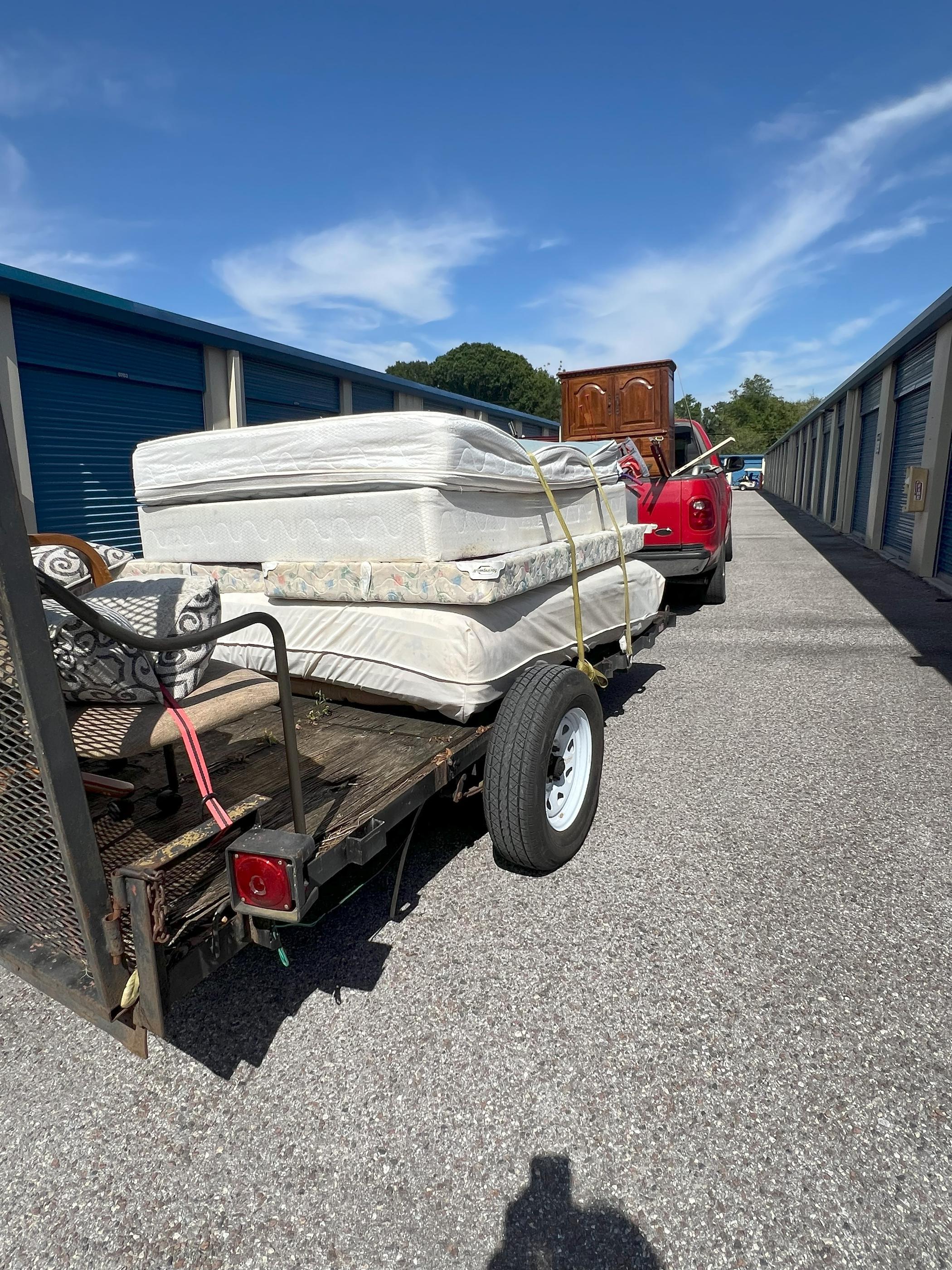 Trailer loaded with old mattresses and furniture that is hitched to a red pickup truck