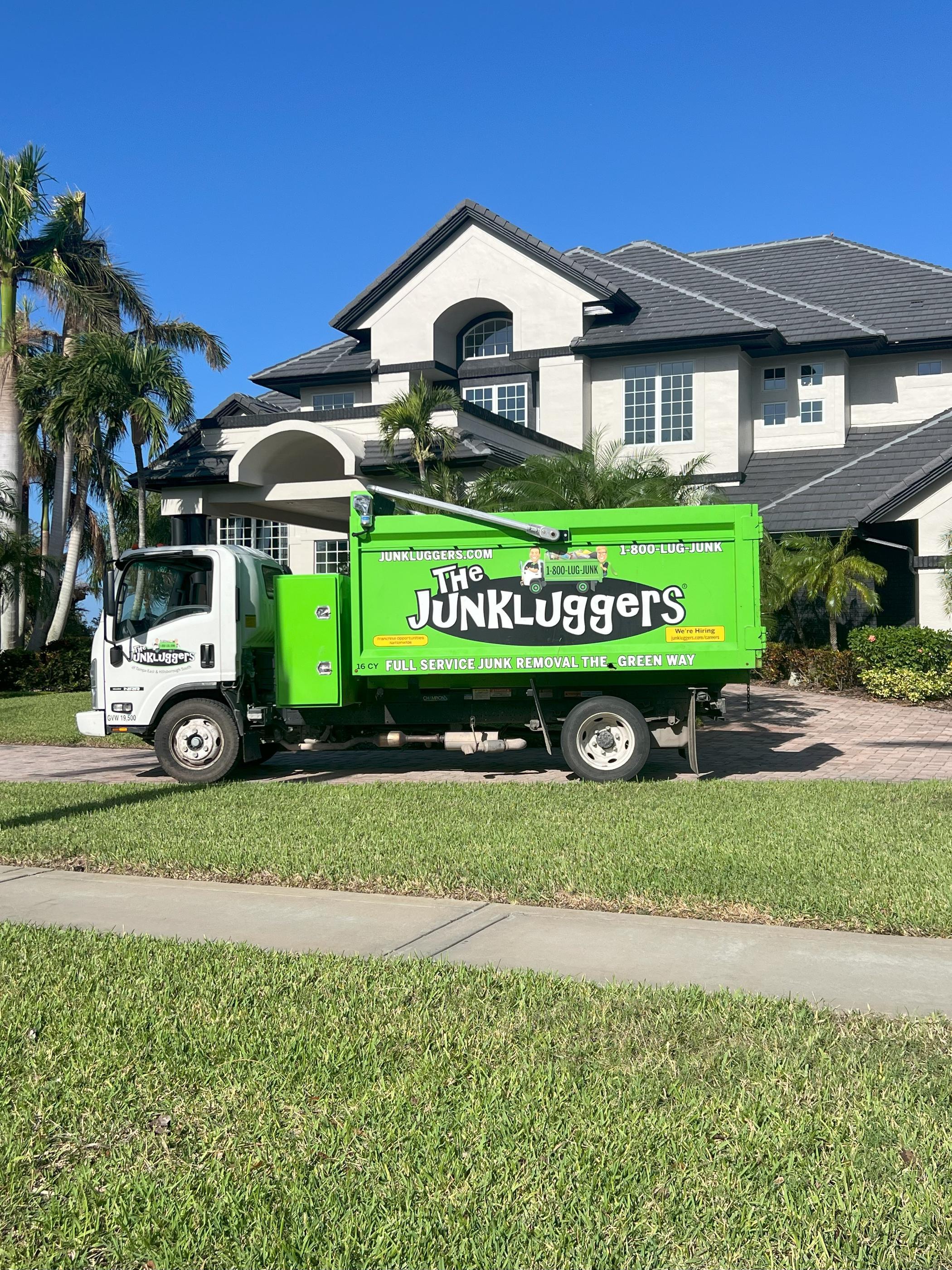 A bright green The JunkLuggers truck parked in front of a large, modern home