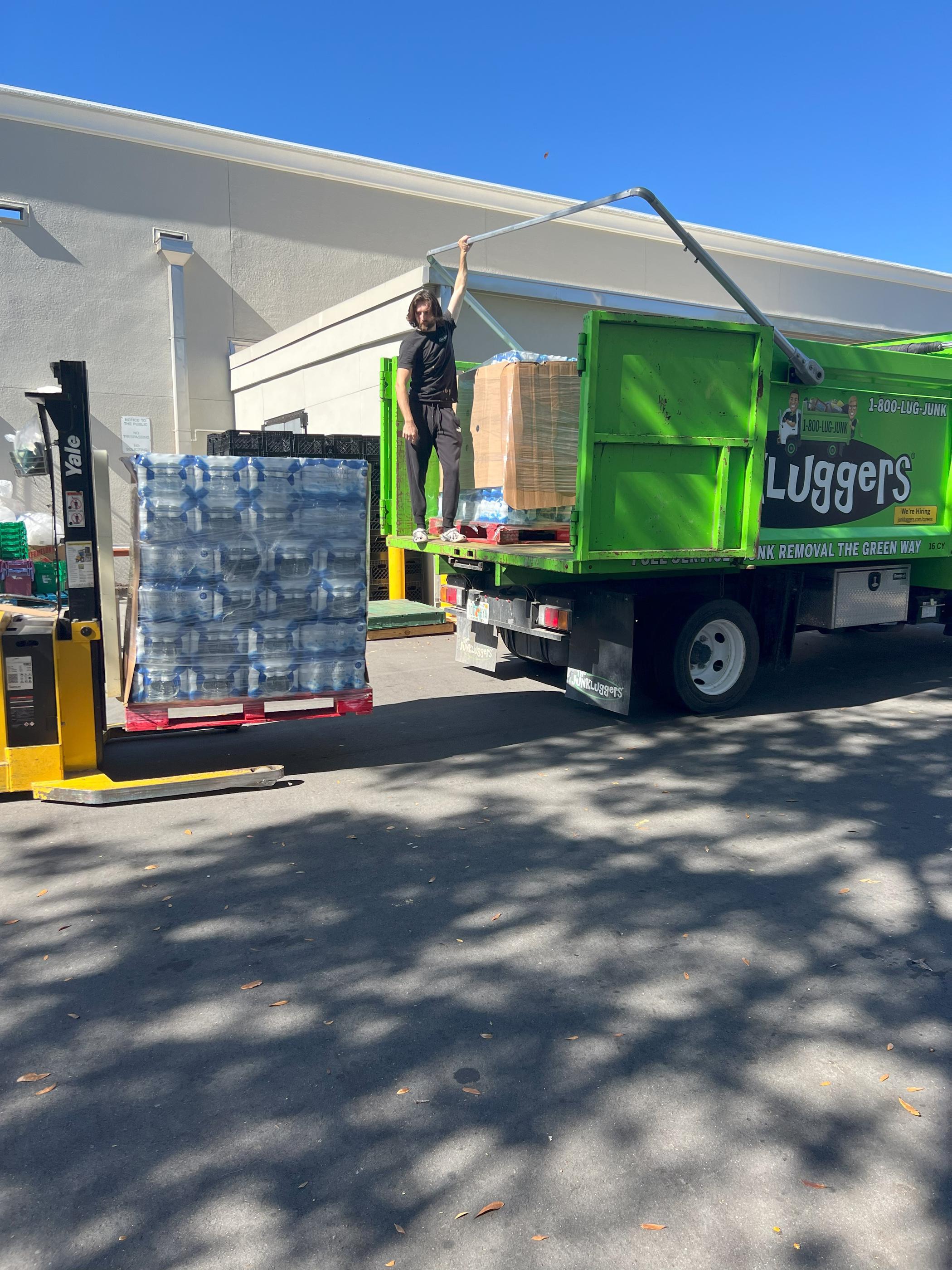 A forklift loading a pallet of bottled water onto a The JunkLuggers truck