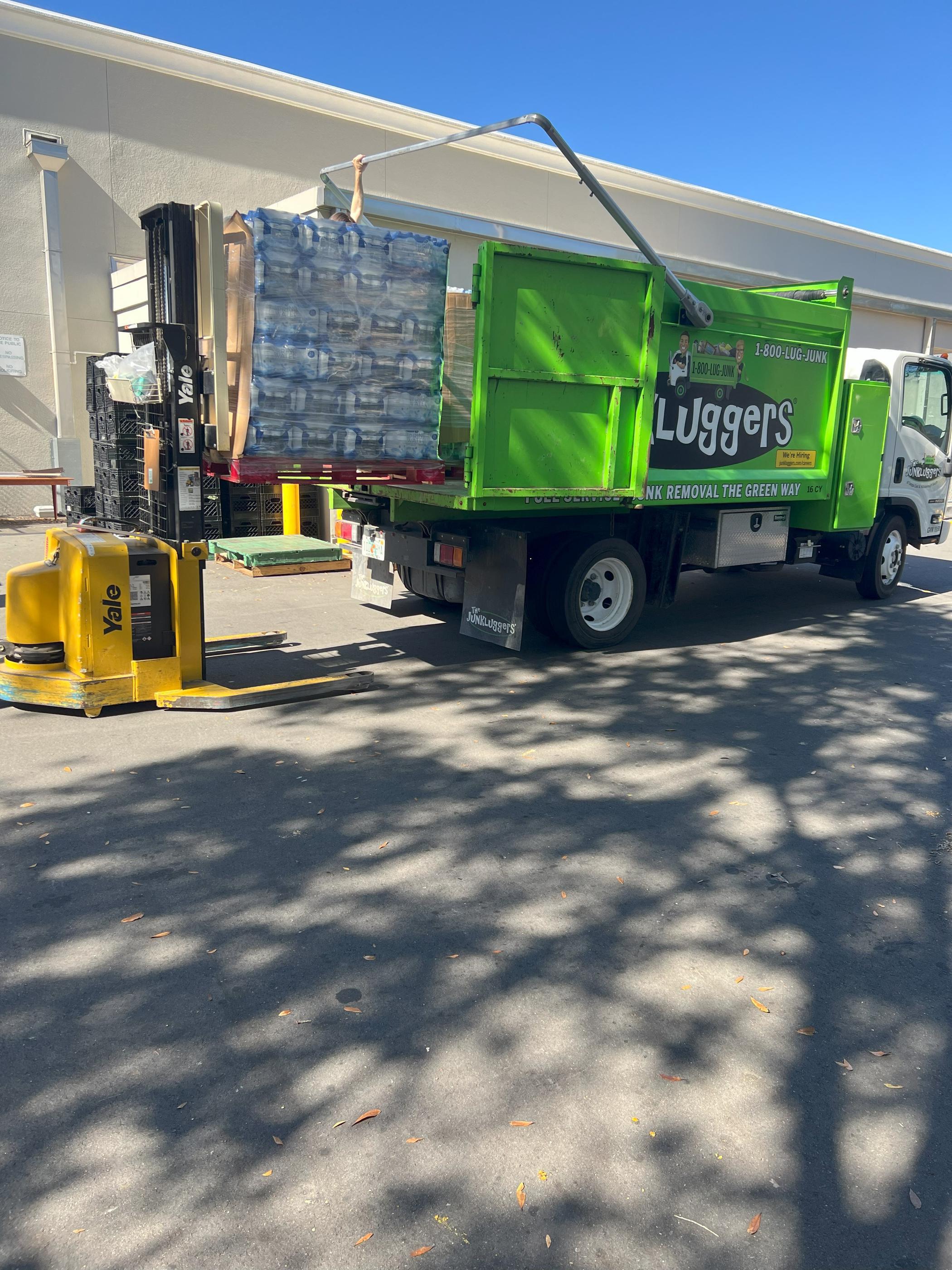 The JunkLuggers truck being loaded with a pallet of bottled water using a forklift