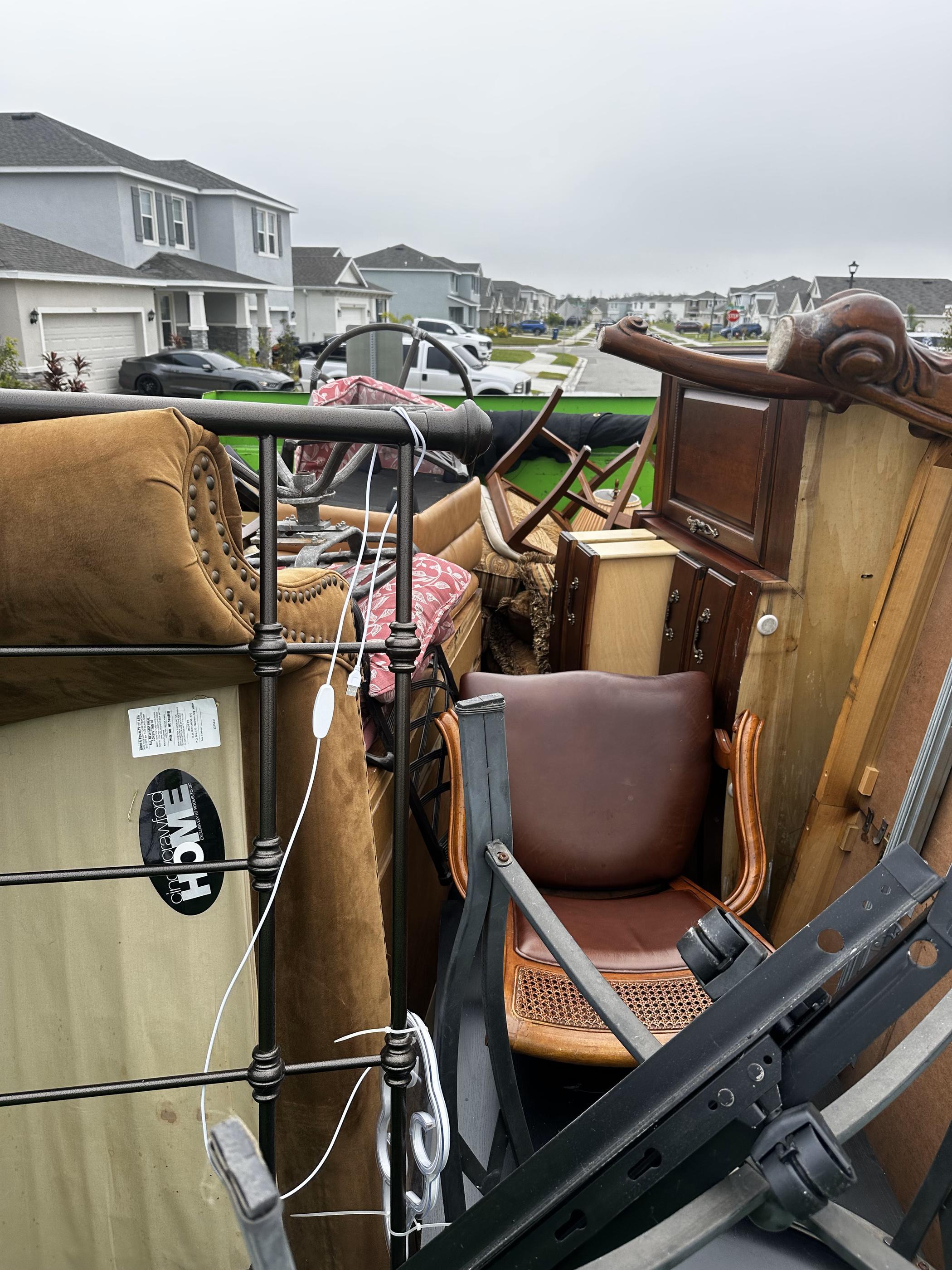 Our truck bed filled with discarded furniture, including a bed frame, chairs, a dresser, and other household items