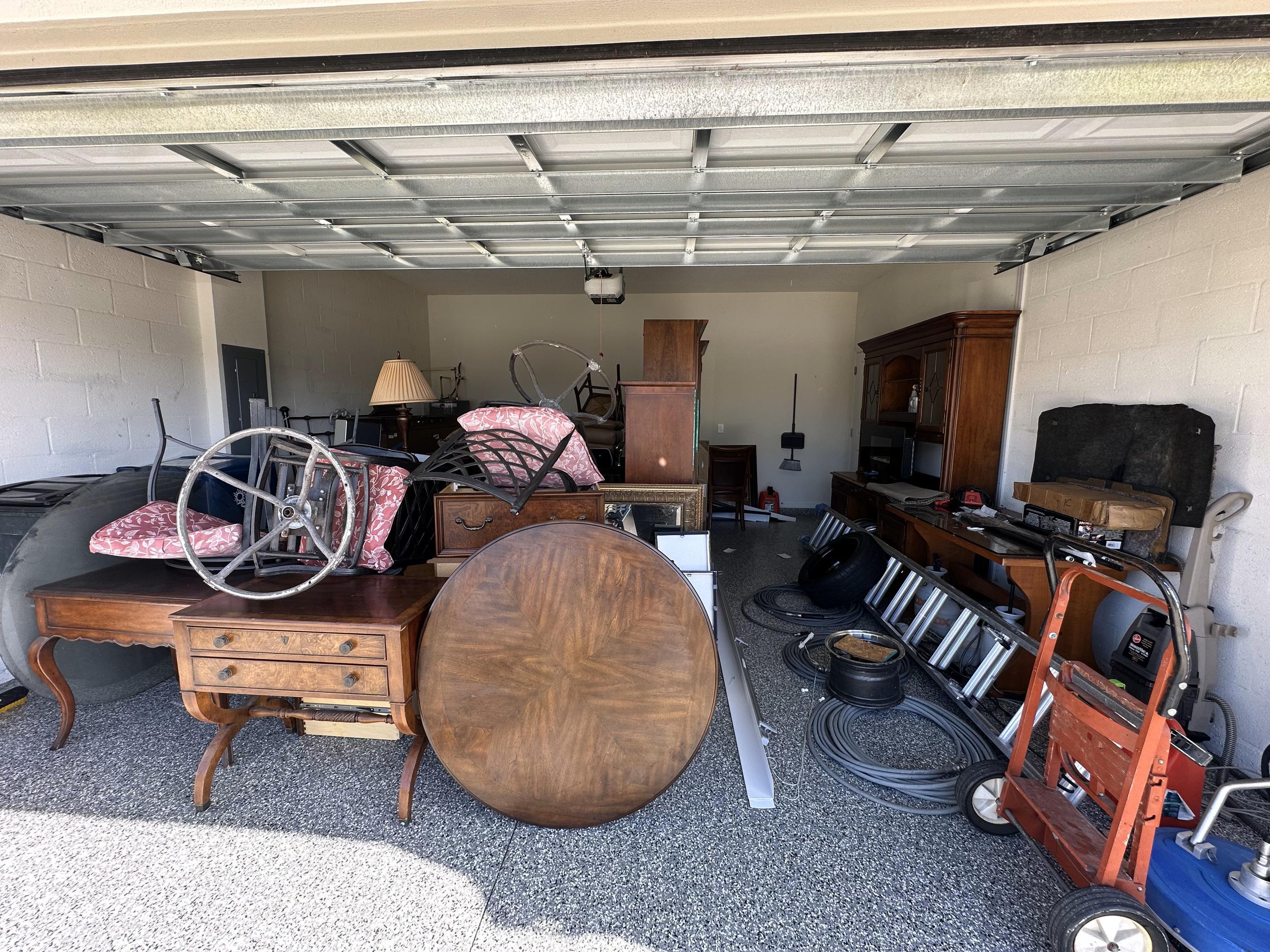 A pile of old furniture, including tables, chairs, a cabinet, a dresser, and various household items