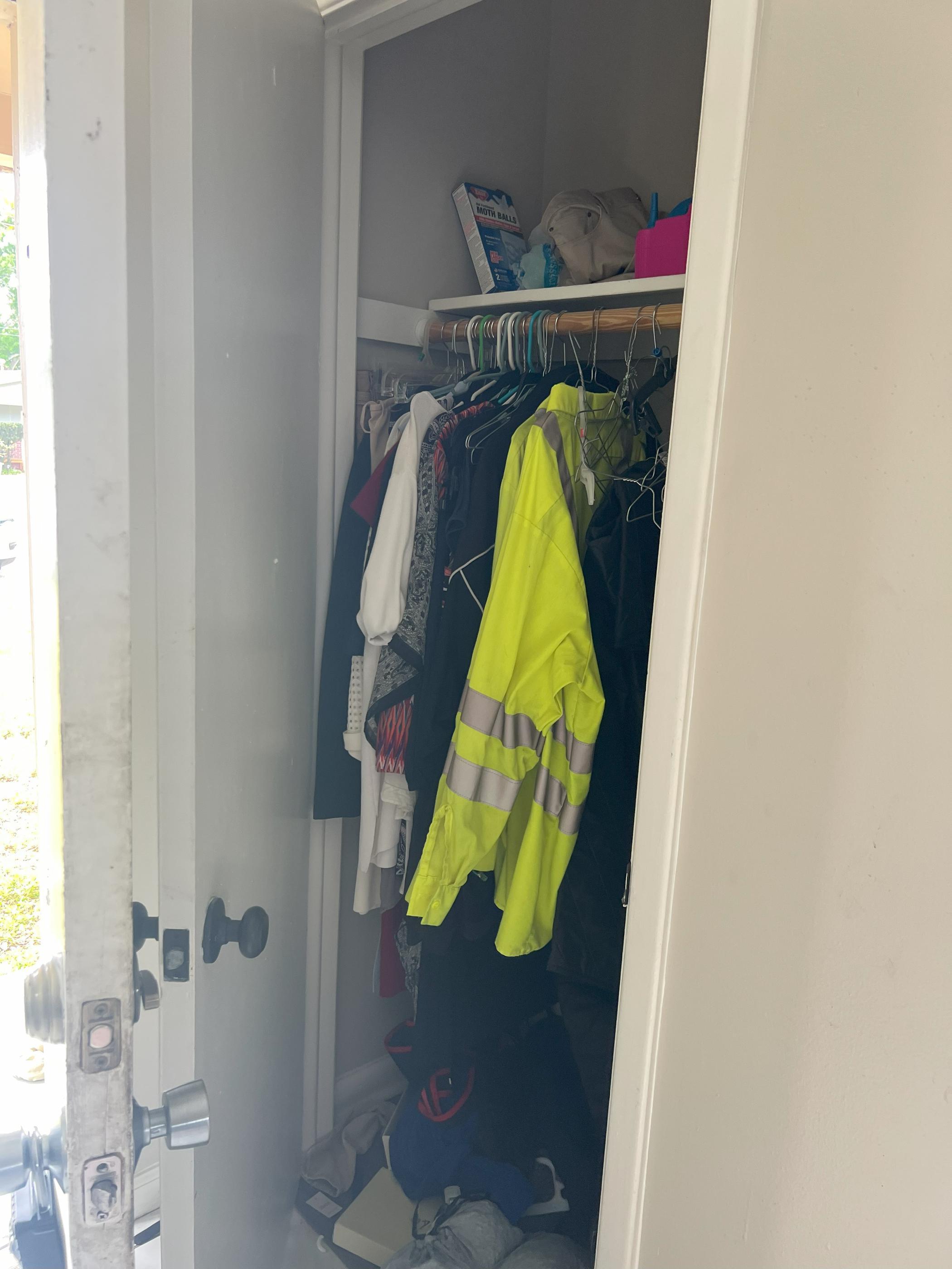 Partially open closet with hanging clothes, including a high-visibility jacket, and shelves with miscellaneous items.