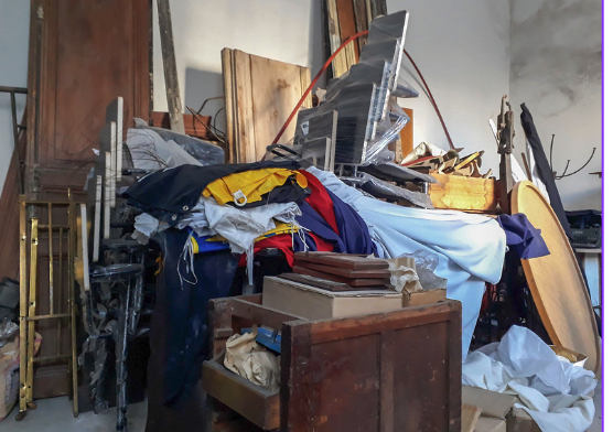 A cluttered garage filled with old furniture, clothes, and miscellaneous items