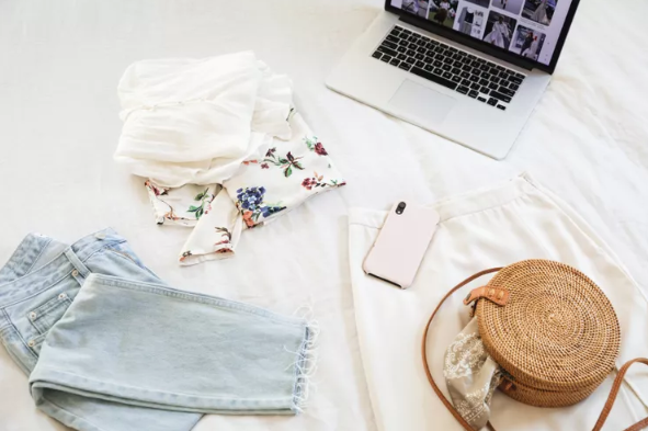 white cloth with clothing, laptop, and purse on top