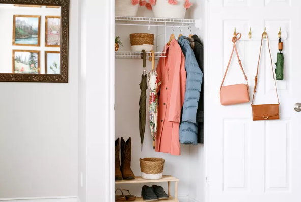 organized closet with coats and umbrellas hanging in it and purses hanging on door