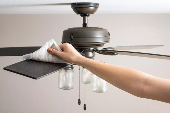 person cleaning the top of a ceiling fan