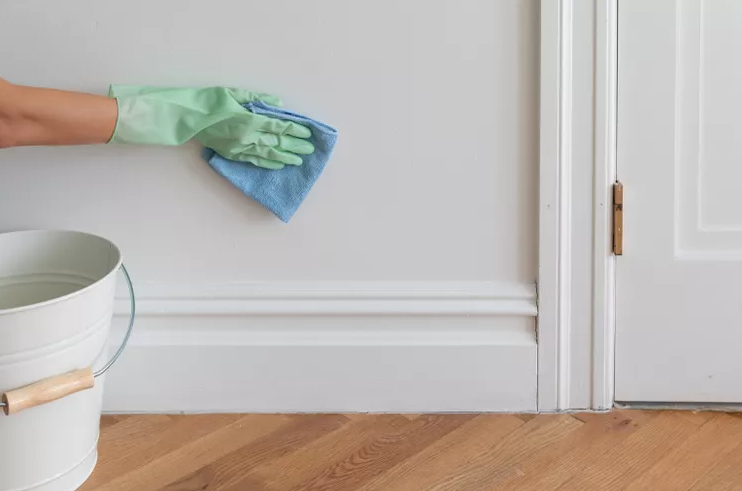 hand in green glove scrubbing wall with blue rag