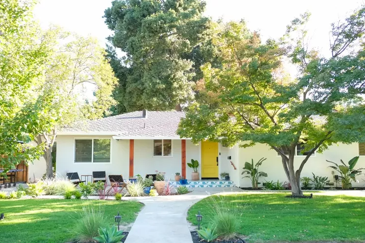 front view of white one story home, with a yellow door and two wood beams