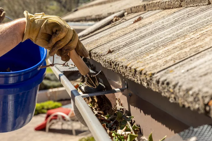 person with work gloves on cleaning gutters